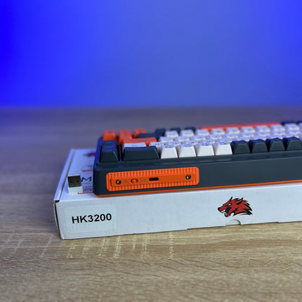Mechanical keyboard on a cardboard box with 'HK3200' branding against a blue gradient background.