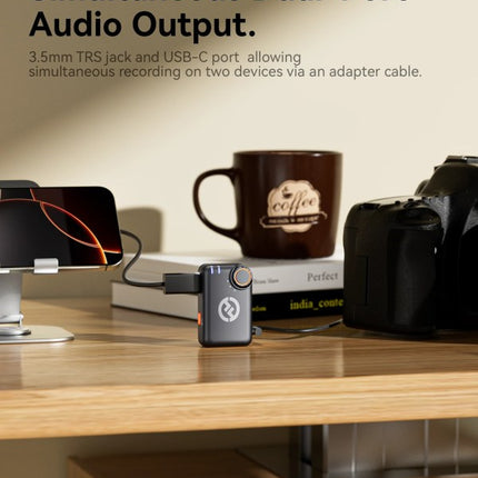 Small audio device on a desk with a coffee mug and phone, featuring text about dual-port audio output.